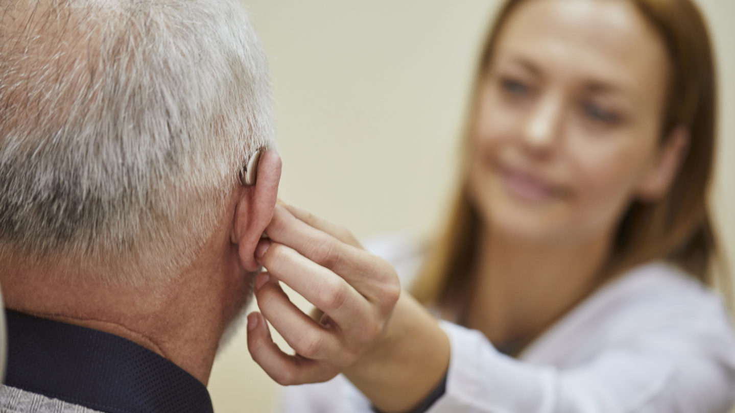 Audiologist fitting a discreet behind-the-ear hearing aid on a patient at ACI Hearing Center